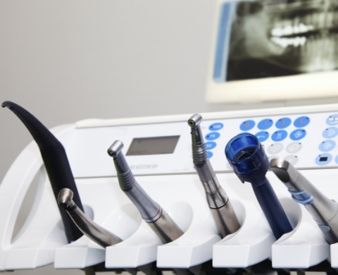 Row of dental instruments with x ray of teeth in background