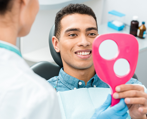 Man in dental chair looking at his teeth in mirror