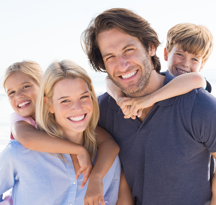 Family of four grinning outdoors on a sunny day