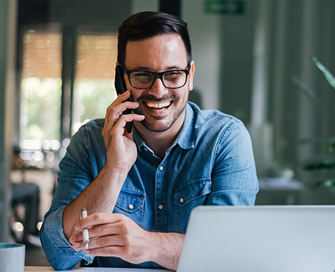 Man in denim shirt smiling while talking on phone