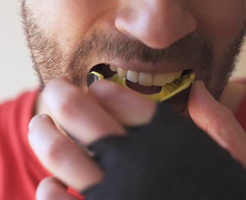 Close up of a man placing a yellow mouthguard into his mouth