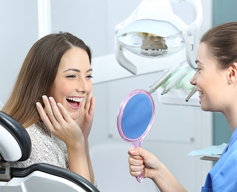 Dental patient admiring her new smile in a mirror