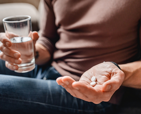 Person holding two pills and a glass of water