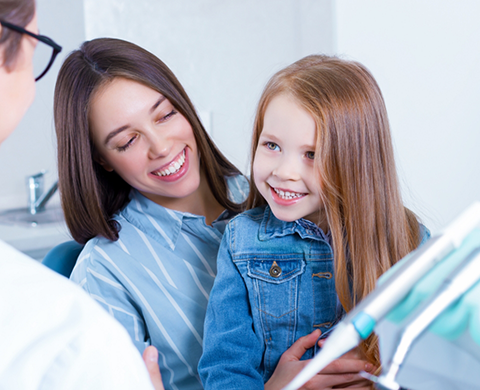 Young girl smiling at the dentist with her mother